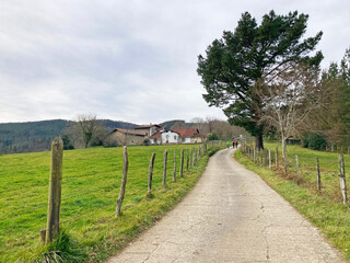 camino carretera paisaje rural de campo con caserio casa de monte con gente senderista montañeras ...