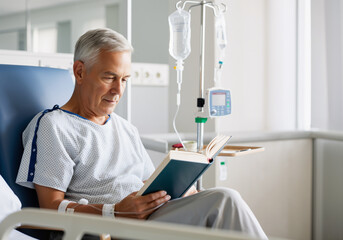 Elderly man finding comfort in reading while receiving intravenous treatment, showcasing resilience and hope during hospital stay