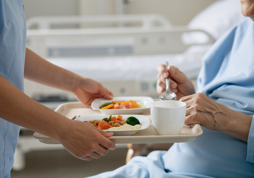 Nurse serving healthy food to elderly patient in hospital room, providing care and assistance with meals