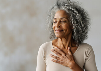Smiling mature woman with gray hair holding hands on chest feeling appreciation and love, showing sincere emotions of gratitude