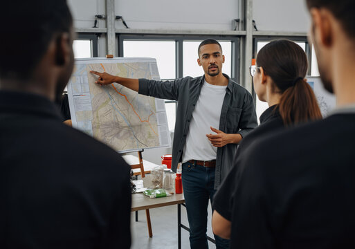 Confident male team leader pointing at map during emergency response training, sharing strategy with diverse team in preparation for disaster relief