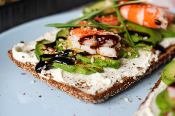 Delicious open-faced sandwich with creamy cheese, avocado, shrimp, and balsamic glaze on whole-grain bread. It is topped with sesame, smoked paprika, and wheat microgreens. A perfect seafood appetizer