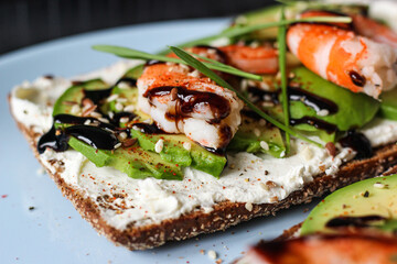 Delicious open-faced sandwich with creamy cheese, avocado, shrimp, and balsamic glaze on whole-grain bread. It is topped with sesame, smoked paprika, and wheat microgreens. A perfect seafood appetizer