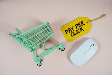 Pay Per Click text on price tag with optical mouse and trolley shopping cart on pink background