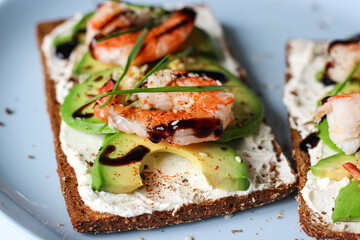 Delicious open-faced sandwich with creamy cheese, avocado, shrimp, and balsamic glaze on whole-grain bread. It is topped with sesame, smoked paprika, and wheat microgreens. A perfect seafood appetizer