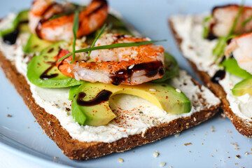 Delicious open-faced sandwich with creamy cheese, avocado, shrimp, and balsamic glaze on whole-grain bread. It is topped with sesame, smoked paprika, and wheat microgreens. A perfect seafood appetizer