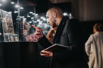 A man examines historical artifacts displayed in a glass case at a museum exhibition, showcasing...