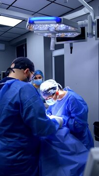 Surgeons work at operating table performing surgery. Chief surgeon leaning above the patient applies metal tool. Vertical video.