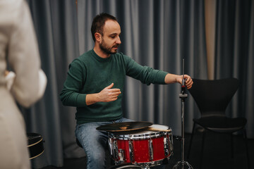 A man adjusts a drum kit component in a music studio environment, focusing intently. The image...