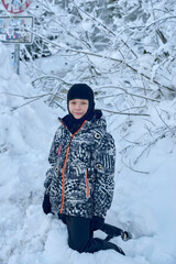 young boy kneeling in a snowy forest wearing a black balaclava and a vibrant abstract patterned...