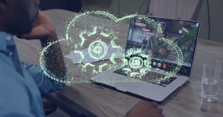 Image of cloud with cogs over african american businessman on laptop image call