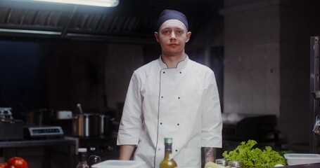 A man in a chef's uniform with a headband smiles while looking at the camera standing in a...