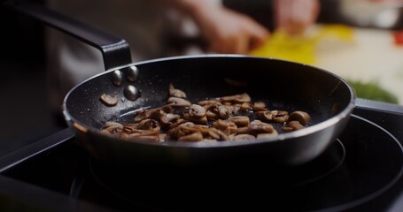 A man in a chef's uniform cuts pepper and adds it to mushrooms frying in a frying pan, close-up of his hands