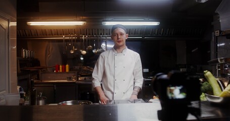 A man in a chef's uniform records the cooking process on video, standing near a frying pan in the...