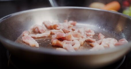 Bacon is fried in a frying pan, tongs stir it, there are no people