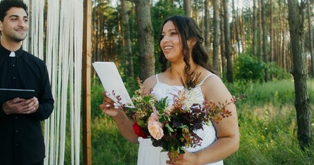 The bride laughs while reading the oath standing opposite the groom in front of the altar with the...
