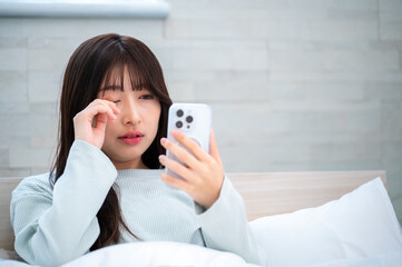 眠そうにスマホを見る日本人女性
