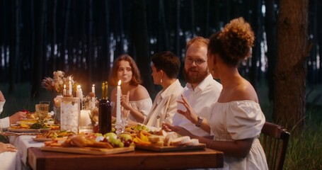 Guests smile and talk while sitting at a beautifully set festive table outdoors at night
