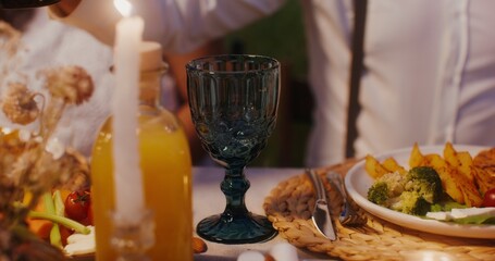A man pours wine into a glass sitting at a beautifully served festive table, close-up of hands, no face