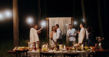 The bride and groom are dancing a slow dance surrounded by their friends at an outdoor wedding...