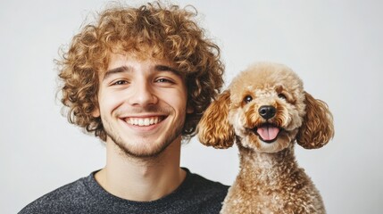 Handsome man with dark curly hair looking at camera and smiling, nearby funny red poodle looking at camera, white plain background