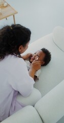 Mom and daughter of African-American appearance laugh and play together on the couch indoors, mom...