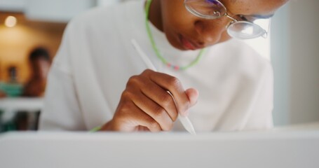 A girl with glasses enthusiastically draws on a digital tablet using a stylus, sitting at a table...