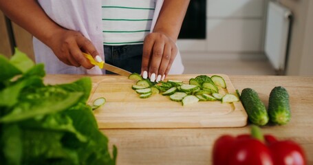 Women's hands are cutting a cucumber while preparing a salad in the kitchen, there is no face