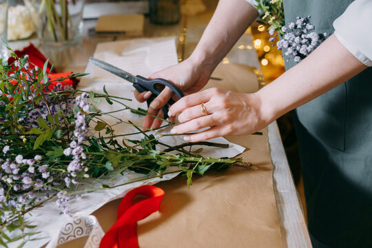 A florist works on preparing beautiful floral arrangement. Various flowers and materials lie on table, emphasizing the artistic and inspiring atmosphere associated with floral design and presentation.