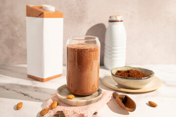 A glass of chocolate protein milkshake rests between a bottle and a milk carton, cocoa.