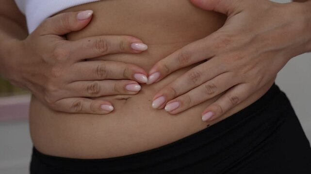 Young woman showing the appearance of white marks on the skin from pressing hands on abdomen, demonstrating bloating and water retention. Swelling, edema caused by fluid retention, hormonal changes