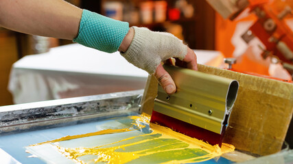 silk screen textile printery. manual screen printing. male hand with a squeegee