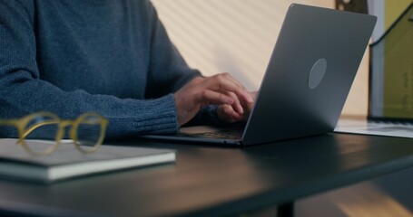 A woman with headphones is typing on a laptop sitting at her desk, working in the office