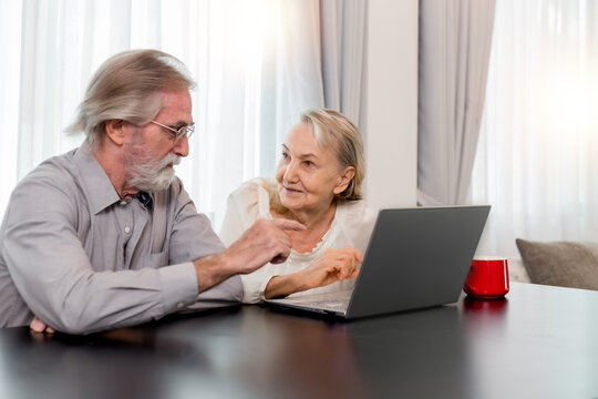 Happy Caucasian 70s mature couple using laptop at home. Old people using computer at home. Senior man and woman surfing the web on a wireless laptop connection. Modern retired lifestyle people.