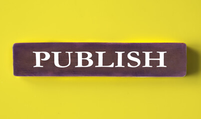 PUBLISH - word on a wooden block close-up on a yellow background