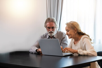 Happy Caucasian 70s mature couple using laptop at home. Old people using computer at home. Senior man and woman surfing the web on a wireless laptop connection. Modern retired lifestyle people.