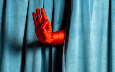 n's hand in a red glove shows an ok sign against a background of blue corduroy curtains