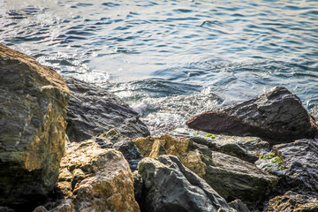A rocky shoreline with a large rock in the foreground. The water is calm and the sky is clear