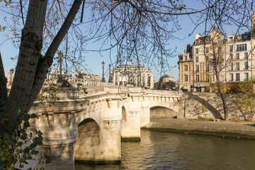 A bridge over a river with a tree in the background in Paris France. The bridge is white and has a shadow on it