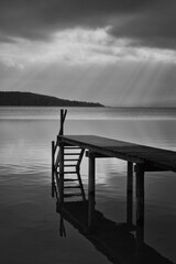 Dramatic clouds over an old jetty at Lake Ammersee with view of the Alps, black and white photo,...