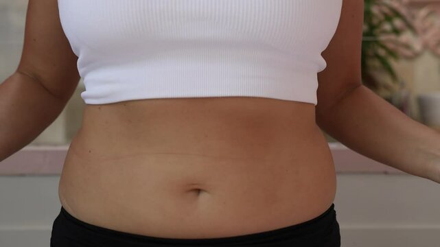 Close-up of a young woman pressing her hands on her abdomen, demonstrating bloating and water retention. Highlighting swelling, edema caused by fluid retention, digestion issues or hormonal changes
