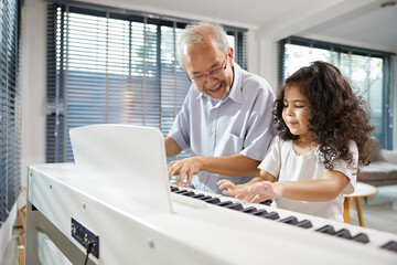 Obraz premium Elderly man teaching his granddaughter to play the piano at home