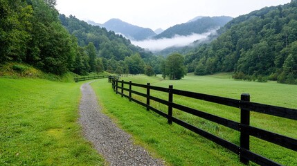 Fototapeta premium Misty Mountain Valley with Path and Fence. Scenic Countryside. Possible Use Stock Photo for Nature, Travel, or Relaxation