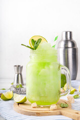 Mojito lemonade alcoholic slush cocktail, garnished with mint and lime slice, summer refreshing slushy drink with vodka, lime juice and mint syrup, on a white table with bar utensils