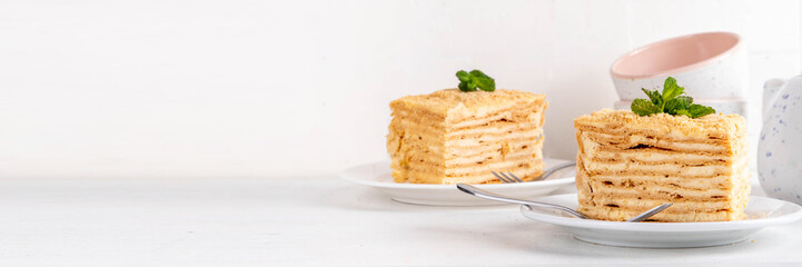 Homemade Napoleon cake slices, layered mille-feuille cake with vanilla creamy custard, tasty delicious puff pastry, on serving plates with forks, copy space