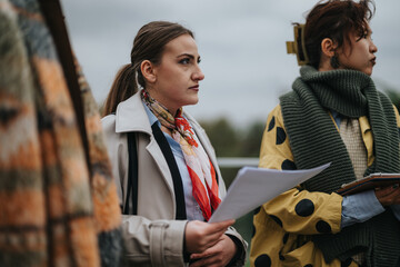 Two women stand outdoors while attending a business meeting, with modern outfits highlighting their...