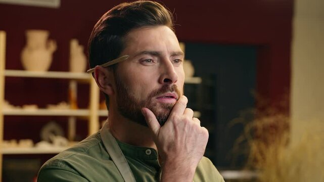 Headshot pondering thoughtful Caucasian artisan bearded man male guy small business owner businessman potter craftsman pencil behind ear think doubt brainstorm planning indoors pottery workshop store