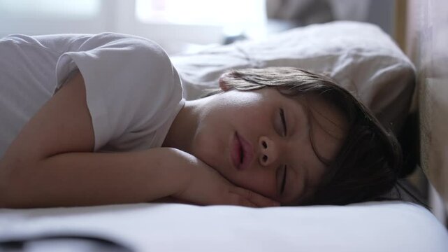 Child sleeping peacefully on a bed, capturing the innocence and calm of childhood slumber, with a soft and serene expression, in a cozy and secure environment