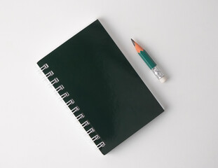 Green spiral notebook and pencil placed on white surface