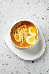 A delicious bowl of noodles soup featuring vibrant broth, tender noodles, and two halved soft-boiled eggs, presented in a minimalist white bowl on a textured surface.